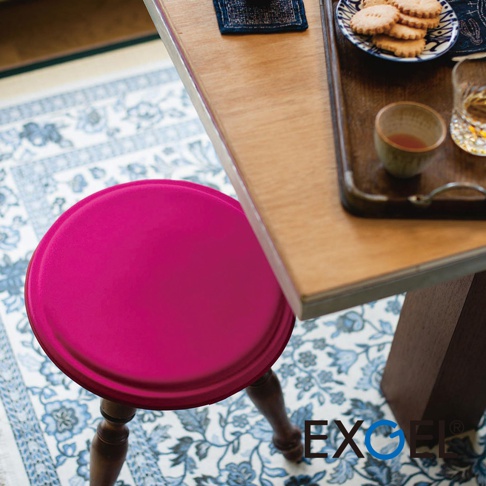 MARU PUNI 圓座墊，採用鮮豔桃紅色圓形座面，搭配木製椅腳，擺放在藍白花紋地毯上，旁有木質托盤，盛有餅乾、茶杯和酒杯。