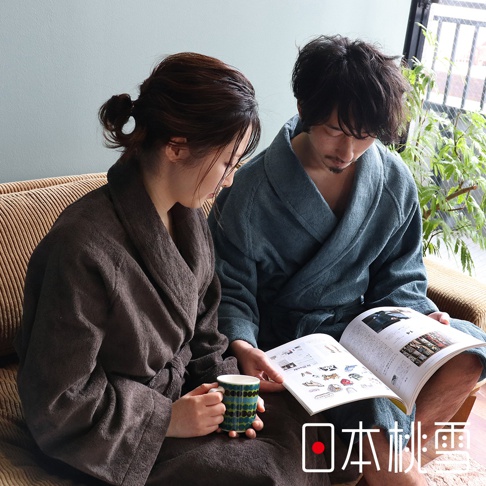 兩位人士穿著深棕色和藍綠色棉質浴袍，坐在沙發上，其中一人手持馬克杯，另一人閱讀雜誌。