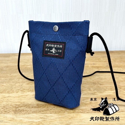 深藍色刺子織手機包，菱格紋樣，黑色束繩，附有品牌標籤。