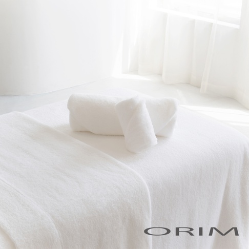 純白色毛巾兩條，一條捲成圓筒狀，另一條對折後呈扇形，擺放在白色毛毯上。