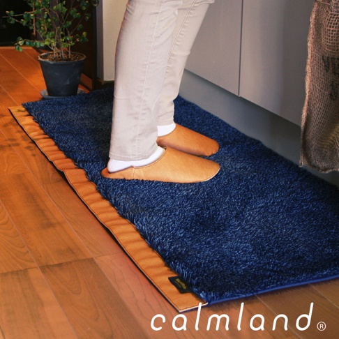 深藍色毛絨廚房地墊，帶有棕褐色邊緣，腳上穿著棕褐色拖鞋，踩在地墊上。