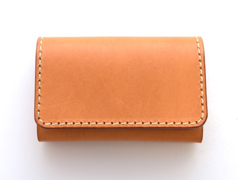 職人手作皮革經典名片收納夾，採用天然皮革材質，呈現溫潤的淺棕色調，邊緣以米白色縫線手工縫製，設計簡潔實用。