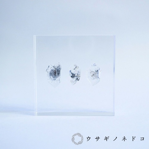 透明壓克力塊內嵌三片天然水晶標本，水晶呈不規則塊狀，帶有灰色及黑色內含物，表面晶瑩剔透。