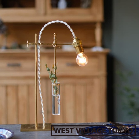 黃銅製一輪花器/燈具展示架，頂部帶有一個燈泡和白色編織電線，中央懸掛著一個玻璃試管花瓶，內有綠色枝葉。