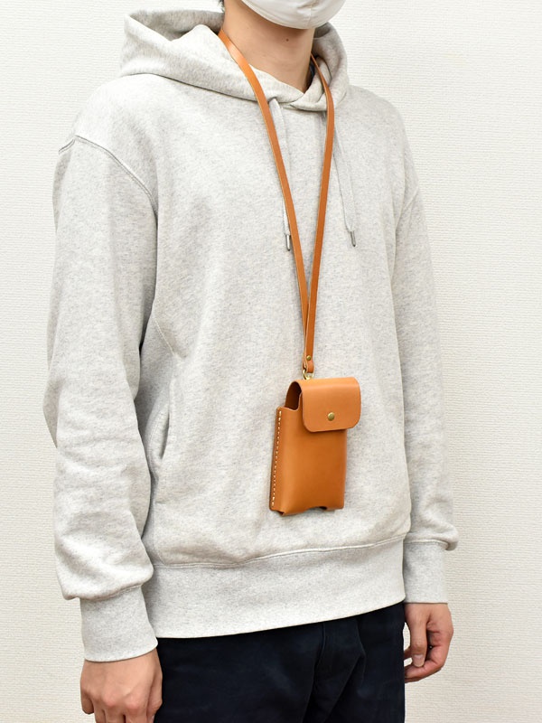 淺棕色皮革製成的手機收納包，帶有啪扣開合的翻蓋，透過一條細長的皮革掛繩掛在頸部。