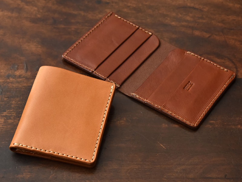 兩個職人手作皮革雙折收納零錢包，一個淺棕色，一個深棕色，皆為真皮材質，縫線清晰。