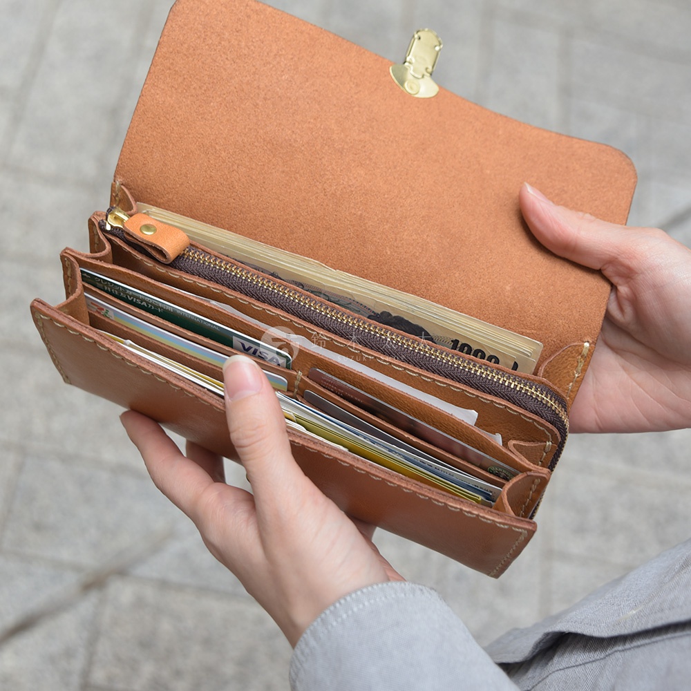 一個棕色皮革長夾，手風琴式多卡層設計，夾內有紙鈔和多張信用卡，由雙手拿起展示。