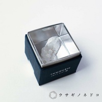 深藍色盒子內，一個銀色金屬框中，陳列著一塊半透明的白色水晶礦石，其表面呈現不規則的晶體紋理。