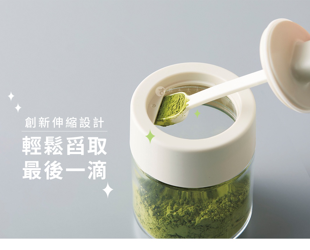 透明玻璃罐裝有綠色粉末，頂部是米白色蓋子，蓋子上的白色量匙正取出粉末，量匙為一體成形設計，勺頭內有綠色粉末。