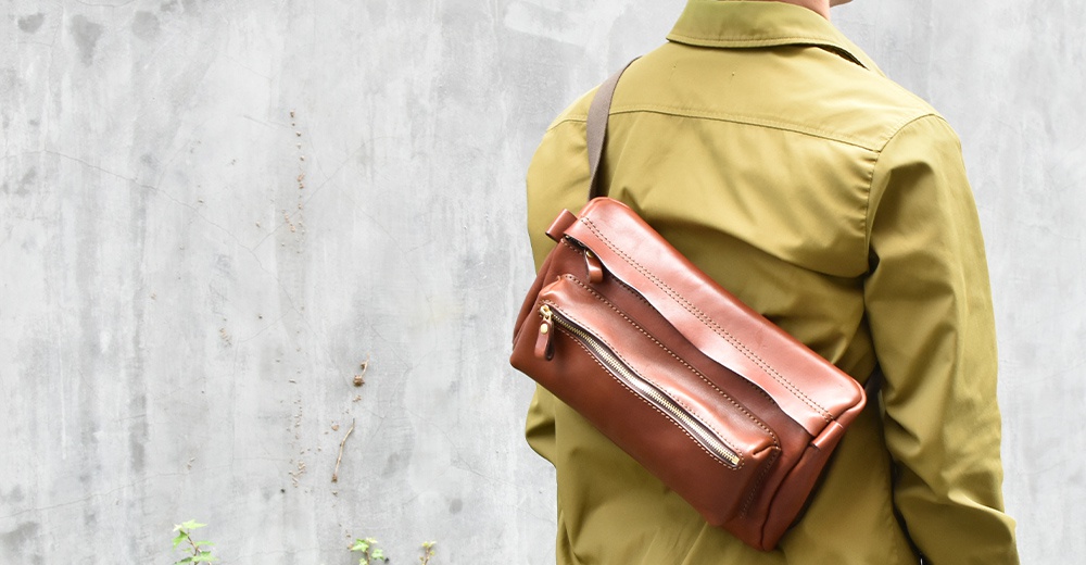 棕色皮革兩用腰掛斜背包，配有金色拉鍊，斜挎於身著卡其色外套的人身上。