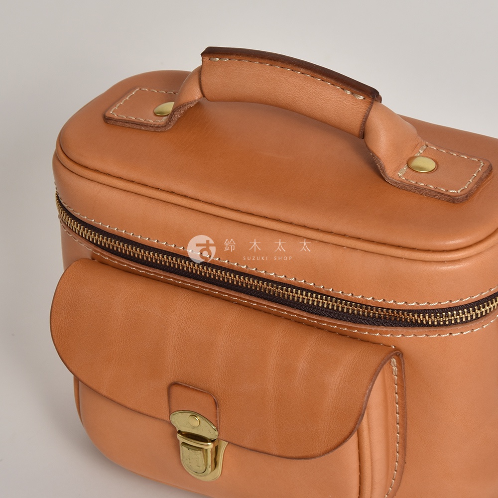 淺棕色皮革相機包，配有頂部提把、拉鍊開合和前方翻蓋口袋，口袋上設有金色金屬扣。