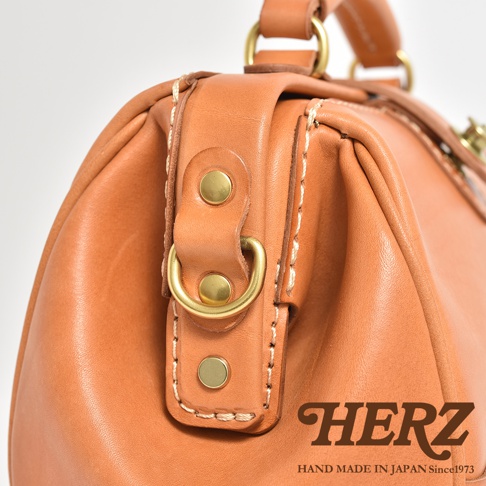 駝色職人手作皮革口金醫生單肩包，特寫包身皮革紋理、黃銅色金屬扣件及縫線細節。