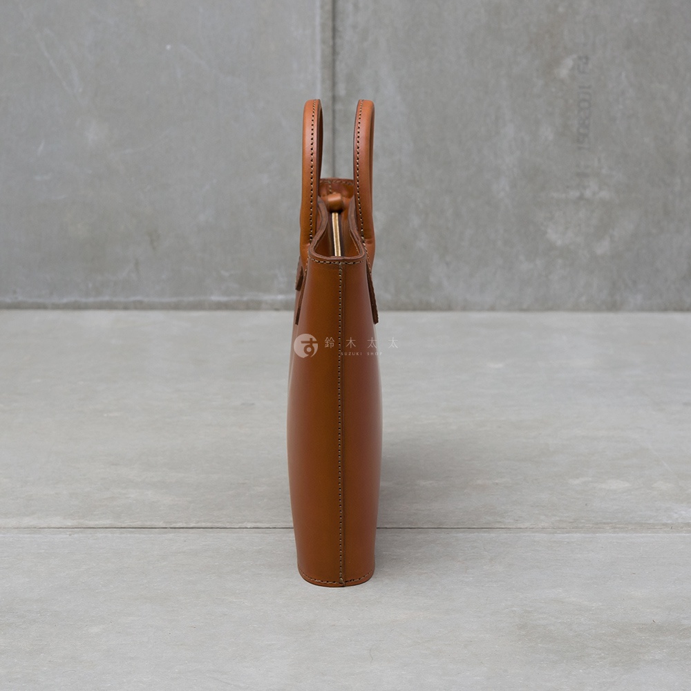 職人手作皮革Organ薄型公事包，淺棕色，兩側對稱提把，金色金屬開口，簡約俐落的箱型設計，整體以皮革壓線縫製，底部有防磨腳釘。