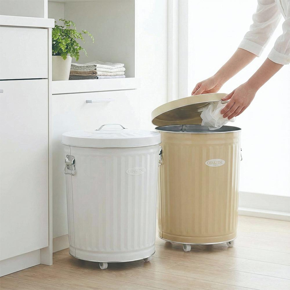 白色和米色 OBAKETSU 圓筒形垃圾桶，其中一個蓋子是打開的，裡面放著一些紙巾