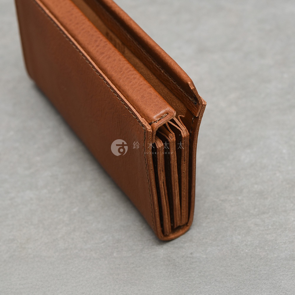一張從側面特寫的日本HERZ職人手作皮革長夾，深棕色皮革具有細緻的自然紋理，側面展示出如同手風琴般的多層次結構設計，上方隱約可見鈴木太太品牌浮水印，整體呈現出紮實且精緻的皮革工藝質感。