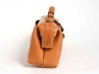 職人手作皮革橫長形單肩包，採用光滑的淺棕色皮革製成，帶有明顯的縫線細節和金色金屬配件。包款側面呈現立體感，強調其結構與質感。