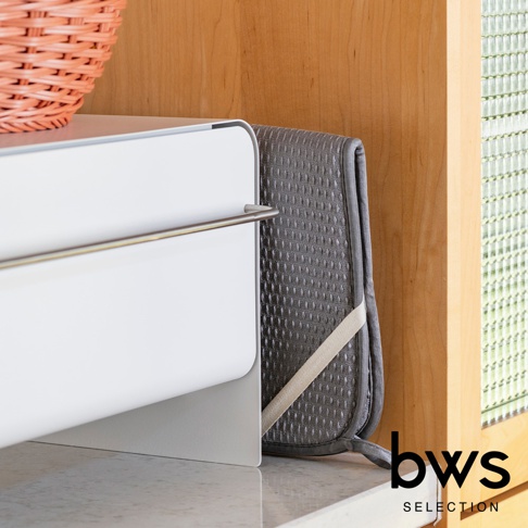 深灰色可折疊收納瀝水墊，表面有菱形紋路，側面有米色綁帶，靠在白色收納盒旁。