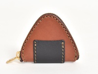 職人手作皮革零錢包，呈現三角形飯糰造型，主體為棕色麂皮，飾有黑色皮革小方塊，並以手工縫線及金色拉鍊裝飾。