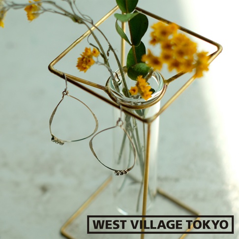 黃銅四角支架搭配透明玻璃試管花器，內插黃色小碎花與綠葉，並掛有兩只銀色水滴形狀耳環。