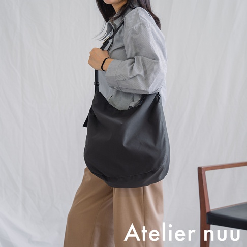 Atelier nuu ssent 肩背托特包，以灰黑色布料製成，搭配卡其色長褲與條紋襯衫，展現簡約穿搭風格。