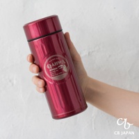 手持一個金屬材質的深紅色保溫杯，杯身光滑，印有QAHWA LOGO。