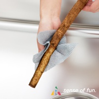 一隻手拿著淺藍色鬆餅紋海綿巾，包裹著一根帶有泥土的牛蒡。