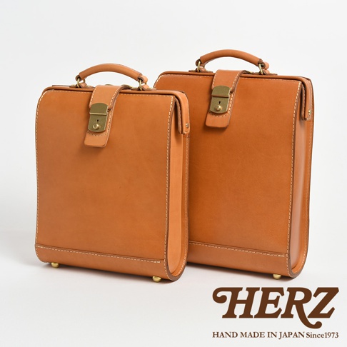 兩款棕色皮革製成的杜勒斯商務後背包，具有復古鎖扣和頂部提把，以及金屬腳釘。