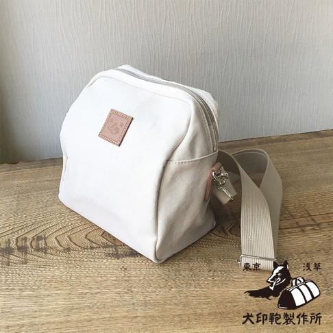 石洗帆布散步包，白色，附有肩帶，包包上有品牌標誌。