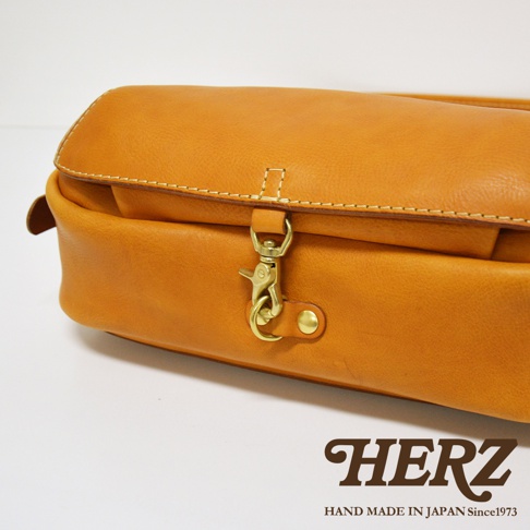 職人手作皮革復古翻蓋郵差包，淺棕色，圓潤的翻蓋設計，配有黃銅色的鉤扣和按鈕，縫線明顯，展現皮革質感。