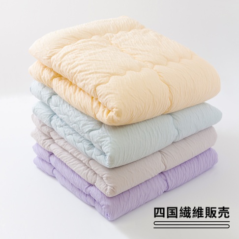 堆疊的舒芙蕾透氣四季被（中棉款），由上至下顏色分別為：淺黃色、淺藍色、淺灰色、淺紫色。被子表面有細緻的紋理，整體呈現蓬鬆柔軟的質感。