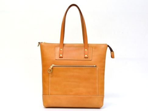 職人手作皮革威靈頓直式拉鍊托特包，呈現天然皮革的溫潤棕色調。包包設計簡潔，正面設有拉鍊口袋，並以精緻的縫線點綴。提把與包身結構穩固，散發質感。