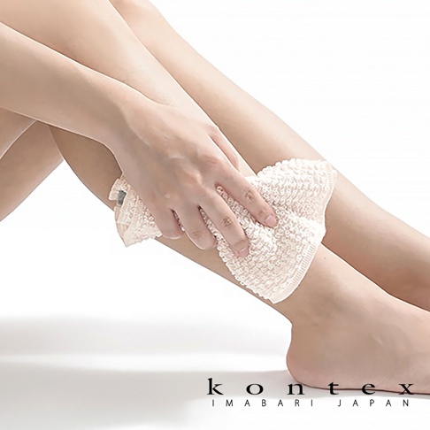 一隻手正拿著淺米色、柔軟的網狀按摩洗澡巾，輕柔擦拭腿部肌膚。