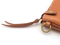 淺棕色皮革短夾，帶有獅鬃風拉鍊，飾有黃銅釦子和圓環，以及皮革製的掛繩。