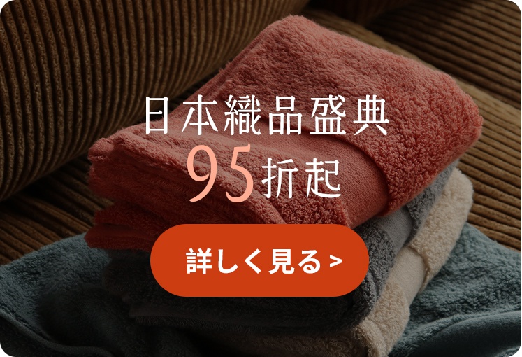 疊放在一起的三條不同顏色毛巾，分別為紅色、灰色與藍色，下方設有一個橘色圓角矩形按鈕，上方文字標示為日本織品盛典九五折起。