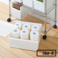 白色寬型整理收納盒，內部裝有六捲衛生紙，盒蓋斜靠在左側。收納盒放置在木質地板上，背景為金屬網架置物架。