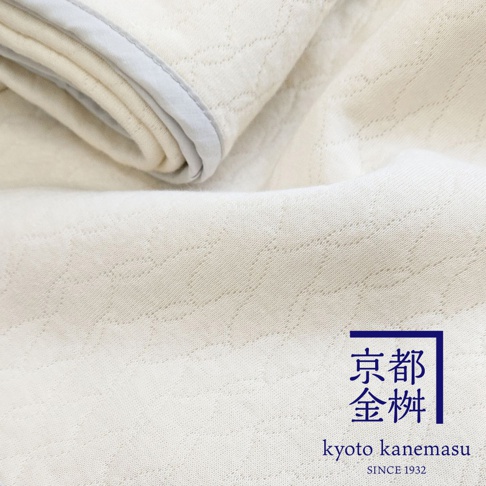 米白色天絲棉絎縫單人毯，織紋細緻，邊緣有淺灰滾邊。右下角有藍色框的日文及英文品牌標誌。