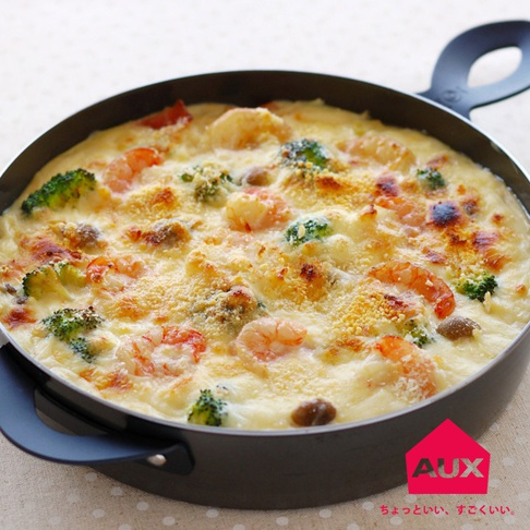 一個裝有焗烤海鮮義大利麵的黑色附蓋小烤鍋，鍋內有蝦仁、花椰菜和濃郁的白醬，表面撒有起司粉並烤至金黃。