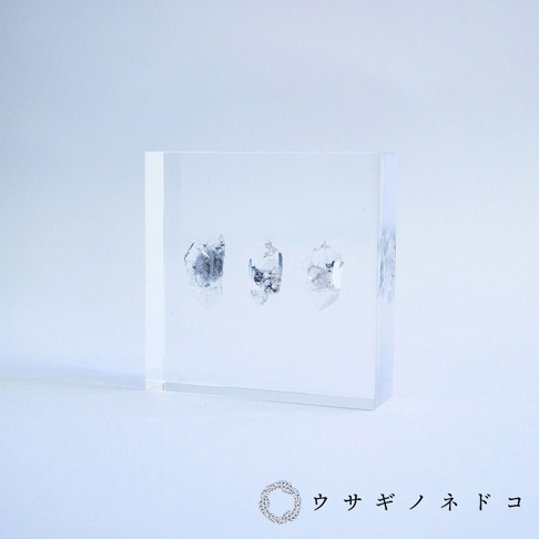 透明樹脂磚塊內嵌三顆半透明的水晶切片標本，水晶呈現天然紋理和部分灰黑色雜質。