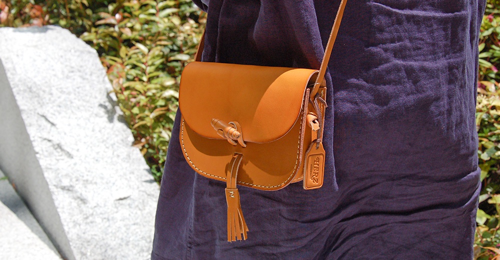 棕褐色皮革製成的職人手作流蘇側背包，帶有竹節狀的旋轉鎖扣和皮革吊牌。