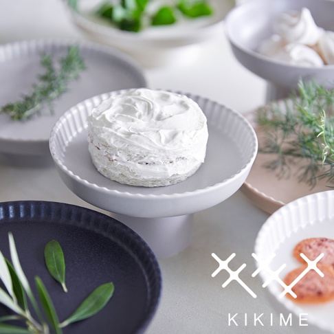 koudai 美濃燒高腳平盤，白色，帶有細緻的紋路，盤面呈現奶油狀的蛋糕，周圍有灰色、粉色及黑色平盤，以及綠色香草點綴。