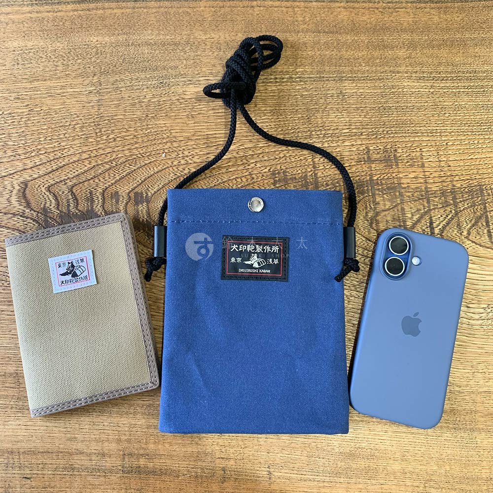 一個犬印鞄製作所的藍色帆布手機包，旁邊放著一個卡其色卡夾和一個手機。