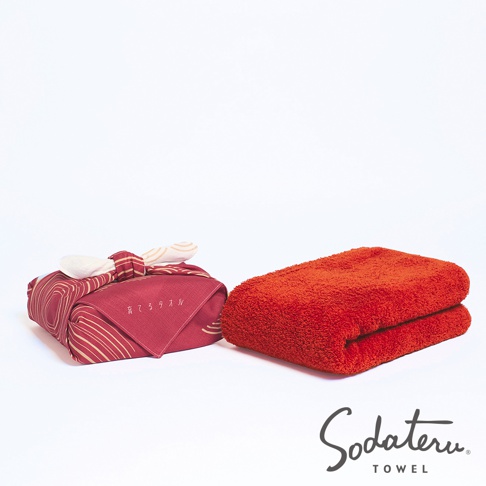 左邊是用和緣紋樣風呂敷包裹的紅色毛巾，右邊是疊放的紅色毛巾，下方有 Sodateru TOWEL 商標