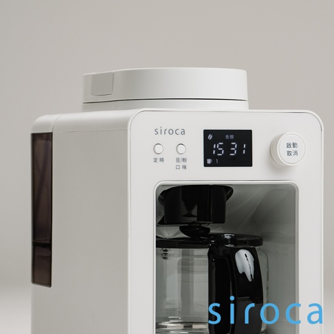 白色 SC-A3520 自動研磨咖啡機，配備黑色把手的玻璃咖啡壺，頂部有圓形蓋子，側面有深棕色透明水箱。機身正面有「siroca」標誌、兩個圓形按鈕、一個顯示時間的黑色數位螢幕，以及一個標有「啟動/取消」的白色旋鈕。