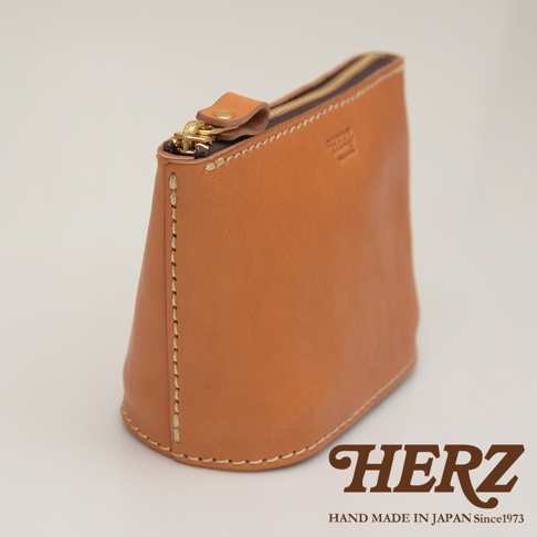 職人手作皮革三角收納包，採用鞣製皮革材質，呈現自然的棕褐色澤。包身為扇形，頂部有金色拉鍊與皮革拉頭，側邊縫線工整，底部呈圓弧狀。