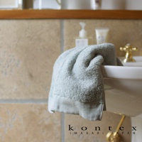 淺藍色超細纖純棉毛巾，蓬鬆柔軟，邊緣有素面滾邊，懸掛在白色洗手台上。