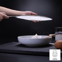 一只手拿著銀色金屬網篩，正在篩濾白色麵粉。麵粉篩入下方白色圓碗中，碗內已有部分麵粉。背景為黑色，畫面右側有雞蛋、木勺和裝有食材的透明罐。