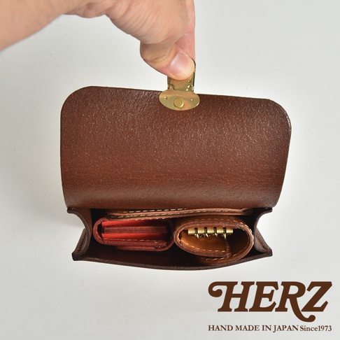 職人手作經典皮革腰包，棕色皮革材質，打開的包蓋上配有金色金屬釦。包內可見紅色卡夾與鑰匙圈。