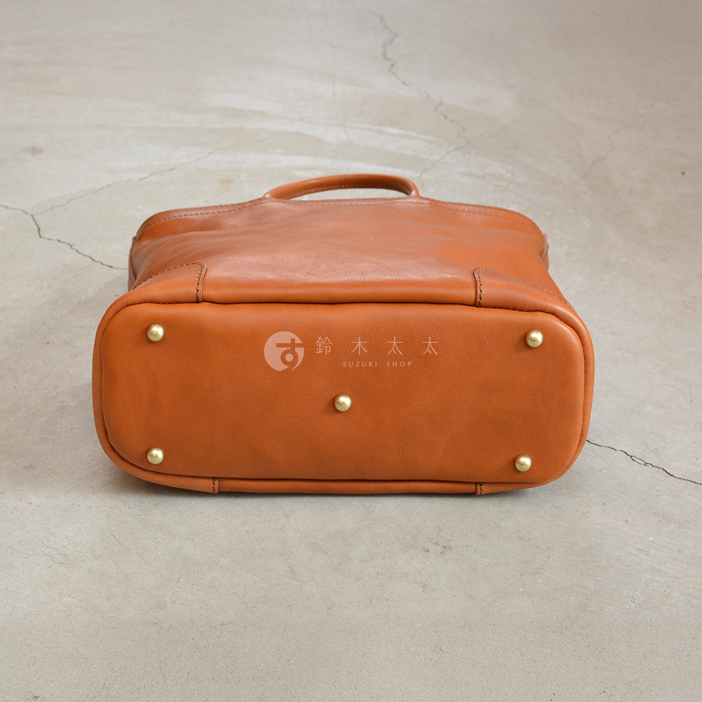 駝色皮革手提包底部，有四個金屬腳釘，中間有「鈴木太太 SUZUKI SHOP」的品牌標誌