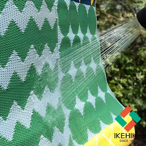 防水 PP 戶外室內兩用收納野餐墊，綠色與白色交織的葉子圖案，材質表面呈現細密的編織紋理，水柱正沖洗在墊子上，展現其防水特性。