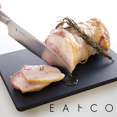 黑色方形砧板上，一片烤肉正被銀色菜刀切下，旁邊有兩片已切好的烤肉。